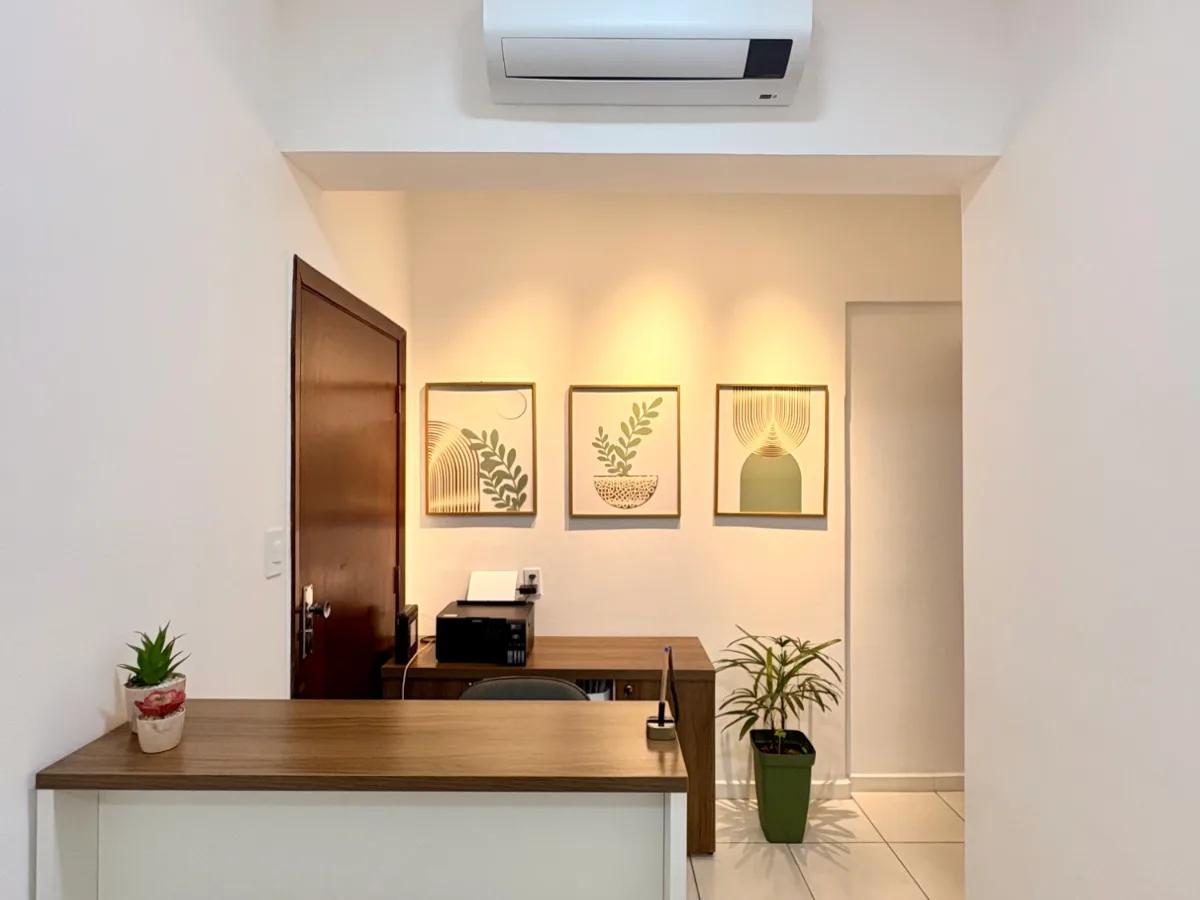 Recepção da clínica, com balcão de madeira, plantas e quadros com ilustrações botânicas